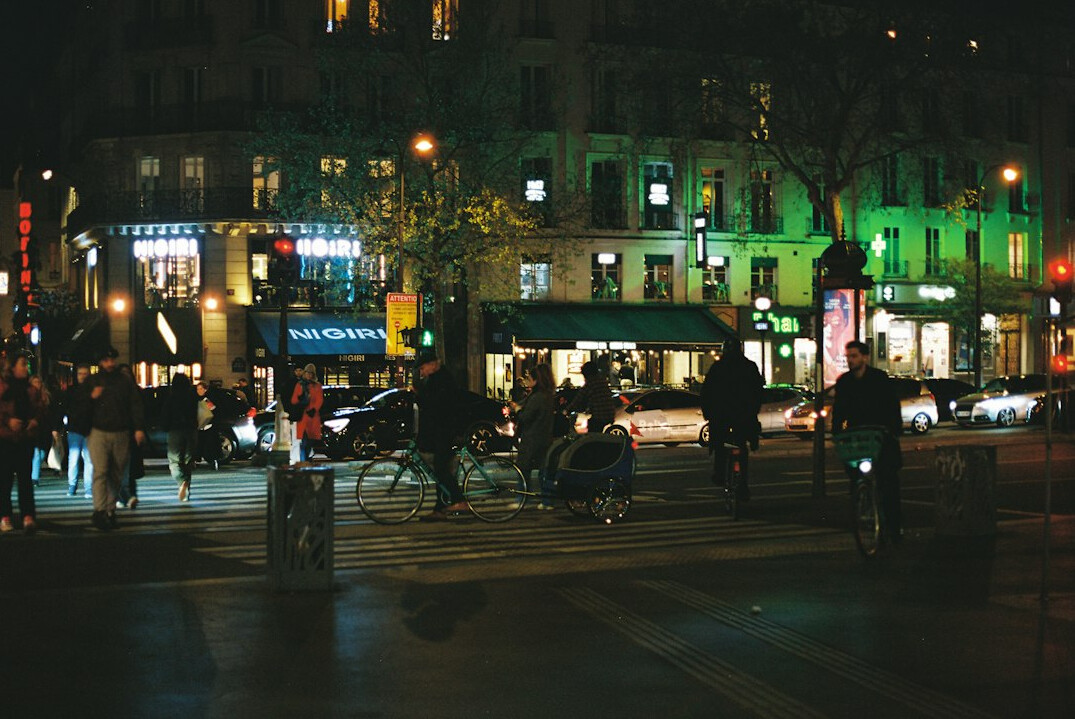 City street illuminated by lights at night with a few pedestrians